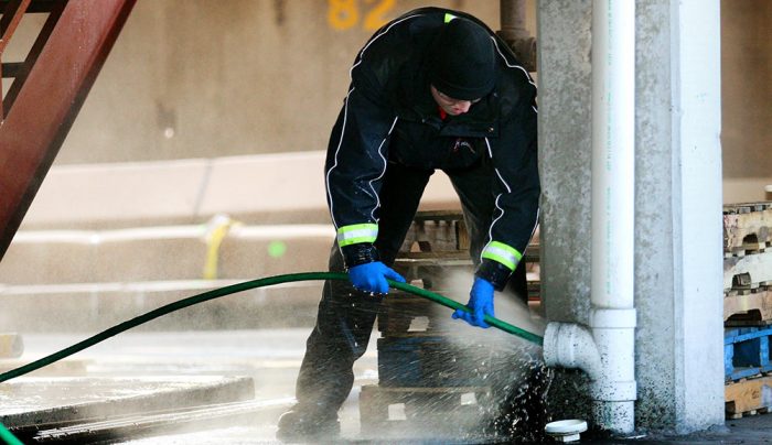 Man spraying water into a pipe using a hydro jetting machine.